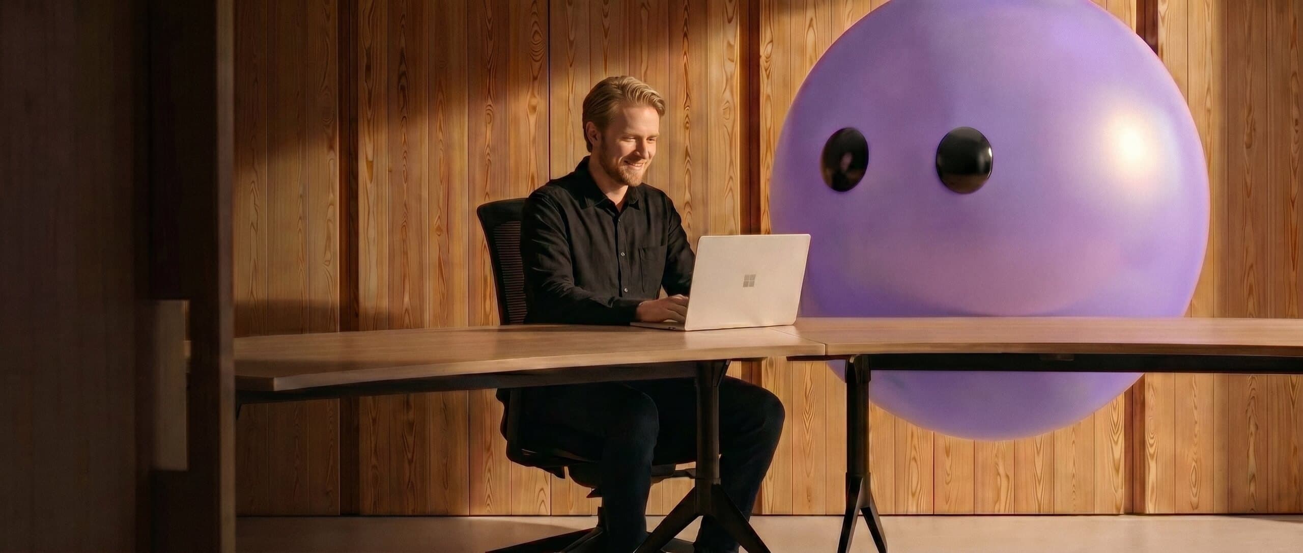 A person working at a laptop beside a large friendly agent orb